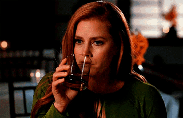 a woman with red hair is drinking a glass of alcohol