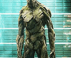 a statue of groot from guardians of the galaxy standing in front of a green wall
