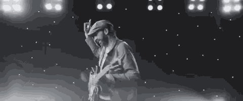 a black and white photo of a man holding a guitar on a stage .