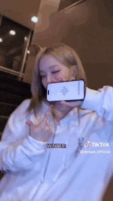 a woman in a white hoodie is holding a cell phone in her hand .