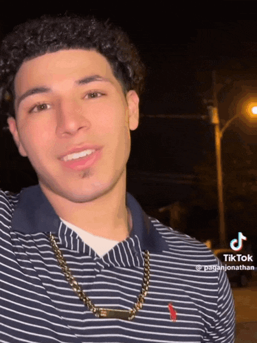 a young man wearing a striped shirt and a gold chain is smiling at the camera .