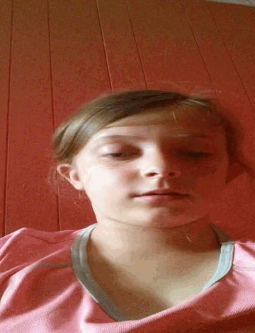 a young girl in a pink shirt looks at the camera with her eyes closed