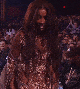 a woman with long hair is standing in front of a crowd wearing a hat that says supreme