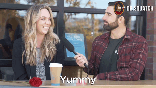 a man and a woman are sitting at a table with a cup of coffee and a sign that says all are welcome behind them