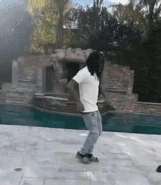 a man in a white shirt and jeans is dancing in front of a pool
