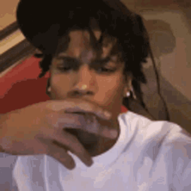a man with dreadlocks is covering his mouth with his hand while wearing a hat .