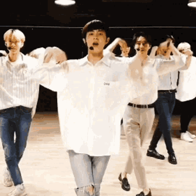 a group of young men are dancing on a stage and one of them is wearing a white shirt that says ove on it .