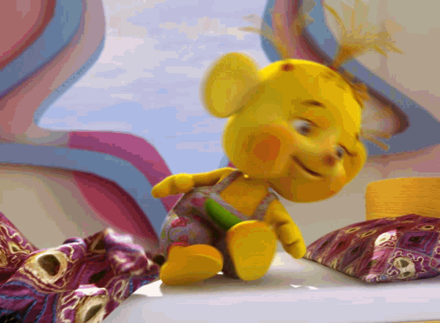 a yellow teddy bear is sitting on a bed with a purple pillow