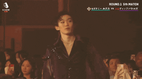 a man stands in front of a crowd with the number 12 visible