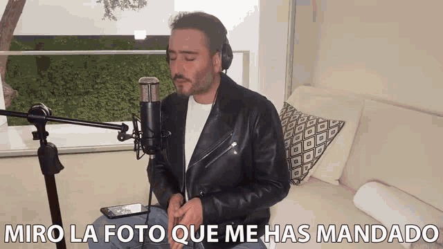 a man in a leather jacket is singing into a microphone with the words miro la foto que me has mandado above him