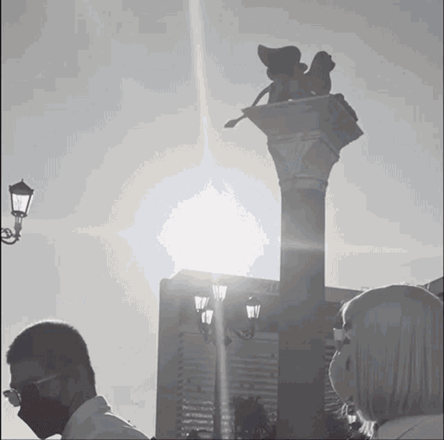 a man wearing a mask stands in front of a statue of a lion on top of a column