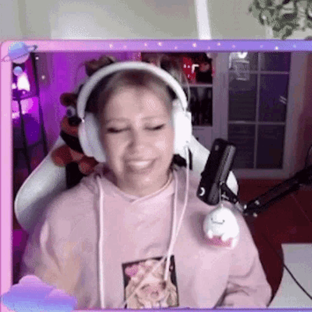 a woman wearing headphones and a pink sweatshirt is sitting in front of a microphone .