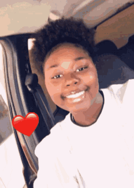 a young woman is smiling in a car with a red heart on her shoulder