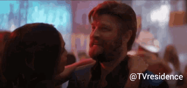 a man with a beard is being kissed by a woman in a bar ..