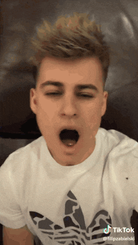 a young man wearing a white adidas shirt is yawning with his eyes closed
