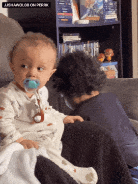 a baby with a pacifier in his mouth sits on a couch next to a boy