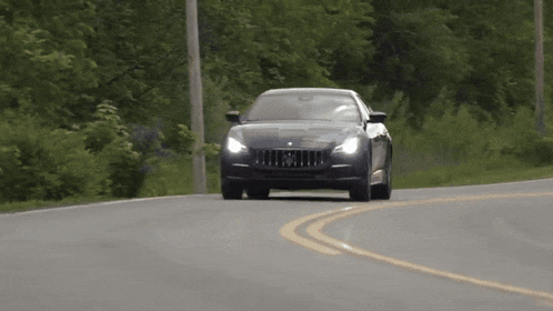 a black maserati is driving down a road with trees in the background