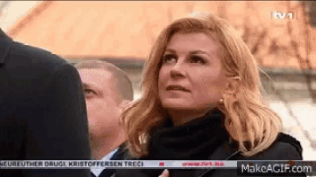 a woman in a black coat stands in front of a tv screen that says rtv1