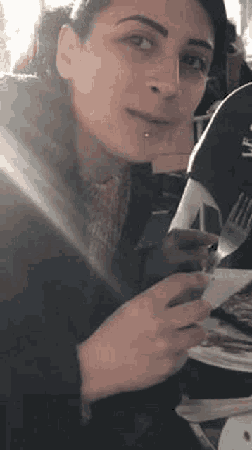 a woman is sitting at a table holding a fork and a napkin .