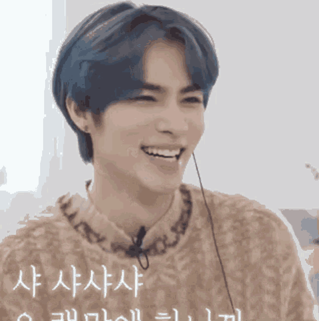 a young man with blue hair is wearing a brown sweater and smiling .