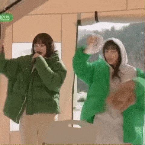 two women in green jackets are singing into microphones while dancing in a tent .