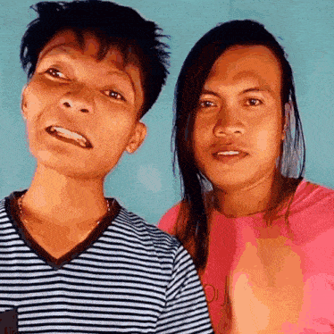 two men with long hair are posing for a picture and one is wearing a striped shirt