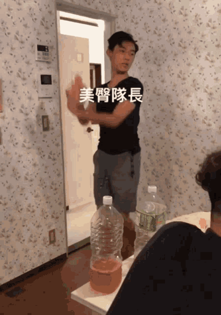 a man in a black shirt is standing in a room with a bottle of green tea on a table