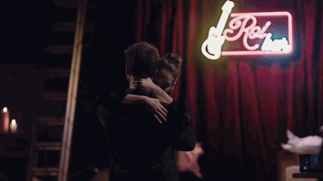 a man and a woman are hugging in front of a neon sign that says rock n ' roll .