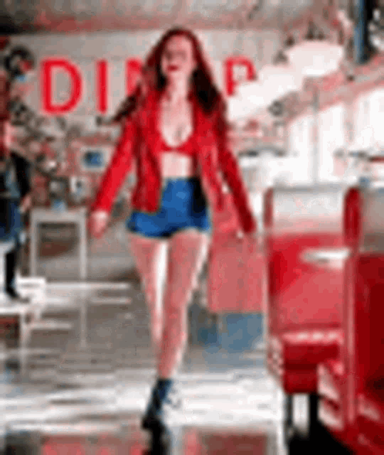 a woman in a red jacket and shorts is walking through a diner .