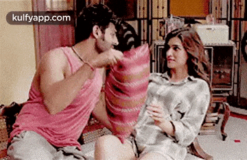 a man and a woman are having a pillow fight while sitting on the floor .