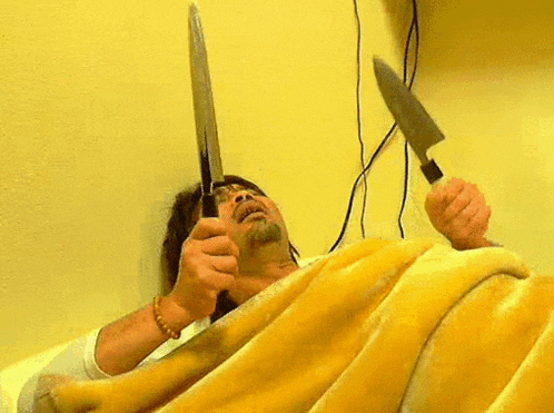 a man is laying on a bed holding two knives