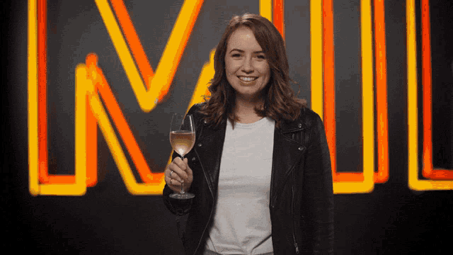 a woman in a leather jacket holds a glass of wine in front of a neon sign that says lnwl