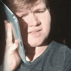 a young man is talking on a cell phone while wearing a gray shirt