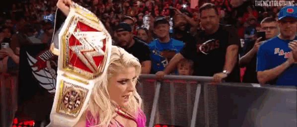 a woman is holding a championship belt in front of a crowd of people .