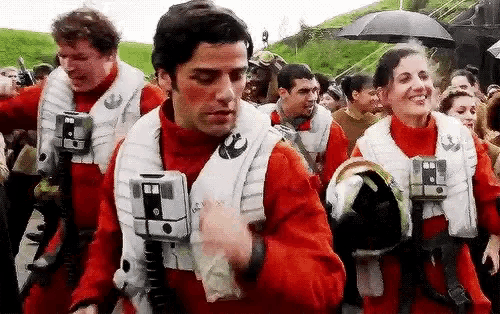 a group of people are standing in a line wearing red jackets and umbrellas .