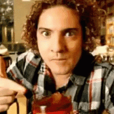 a man with curly hair wearing a plaid shirt is drinking from a cup