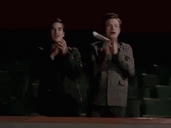 two men are clapping in a theater with the word bravo written on the screen .