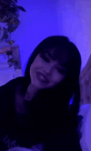 a woman is laying on a bed in front of a blue light and looking at the camera .
