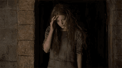 a woman with long red hair is sitting in a dark room with her hand on her forehead .