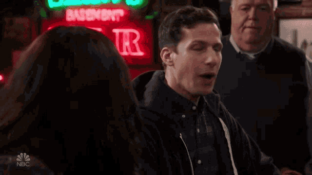 a man is laughing in front of a neon sign that says bar