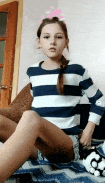 a girl wearing a striped shirt and shorts sits on a bed