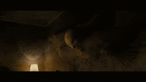 a woman laying on a bed in a dark room with a clock on the wall