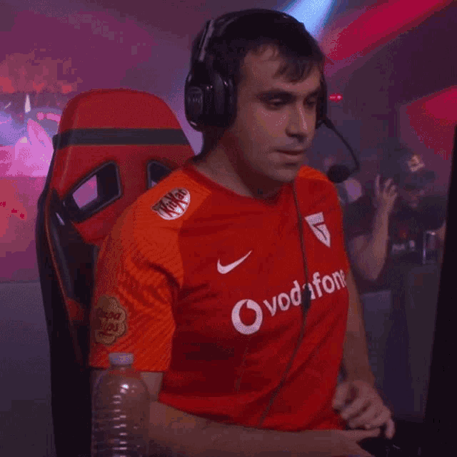 a man wearing headphones and a red vodafone shirt holds a controller