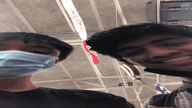 a man wearing a mask smiles next to another man wearing a mask