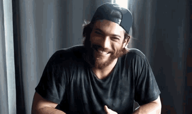 a man with a beard wearing a baseball cap and a black shirt is smiling