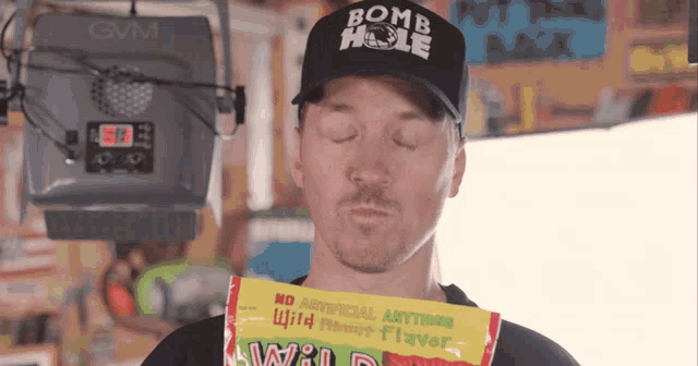 a man wearing a bomb hole hat is holding a bag of wild berry flavored candy