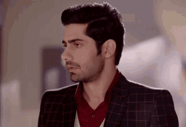 a man wearing a suit and a red shirt looks to the side