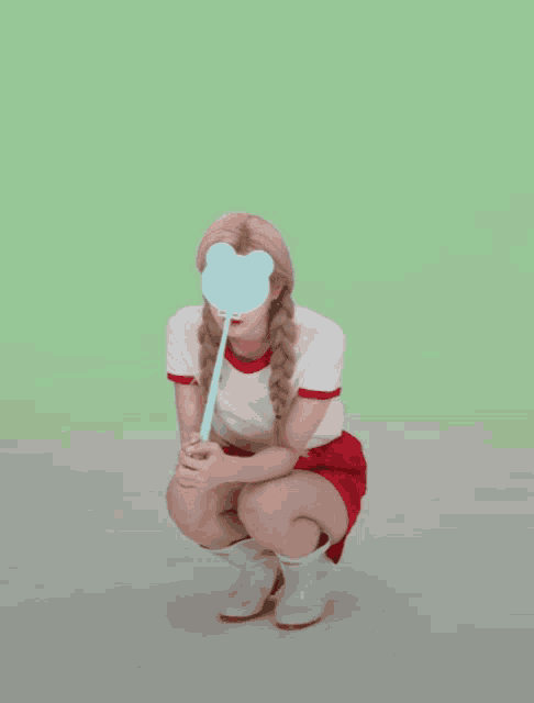 a girl in a red skirt is squatting down holding a blue heart