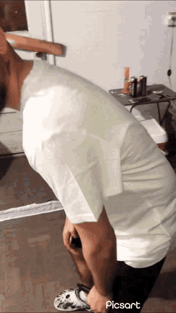 a man in a white shirt is kneeling down in front of a mirror with picsart written on the bottom