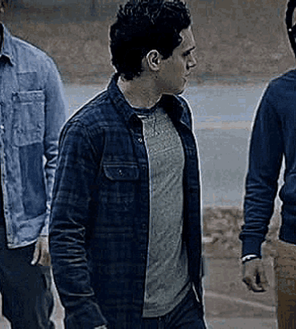 a man in a plaid shirt is standing next to two other men in denim shirts .